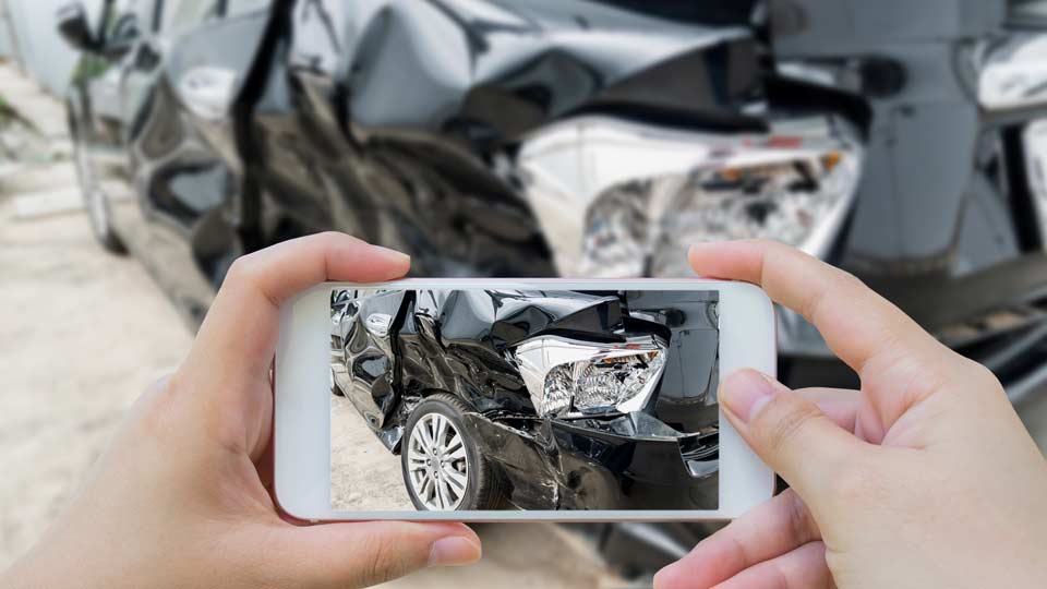 Unfallwagenankauf Daun: Unfallschaden an einem Auto wird mit dem Smartphone fotografiert.
